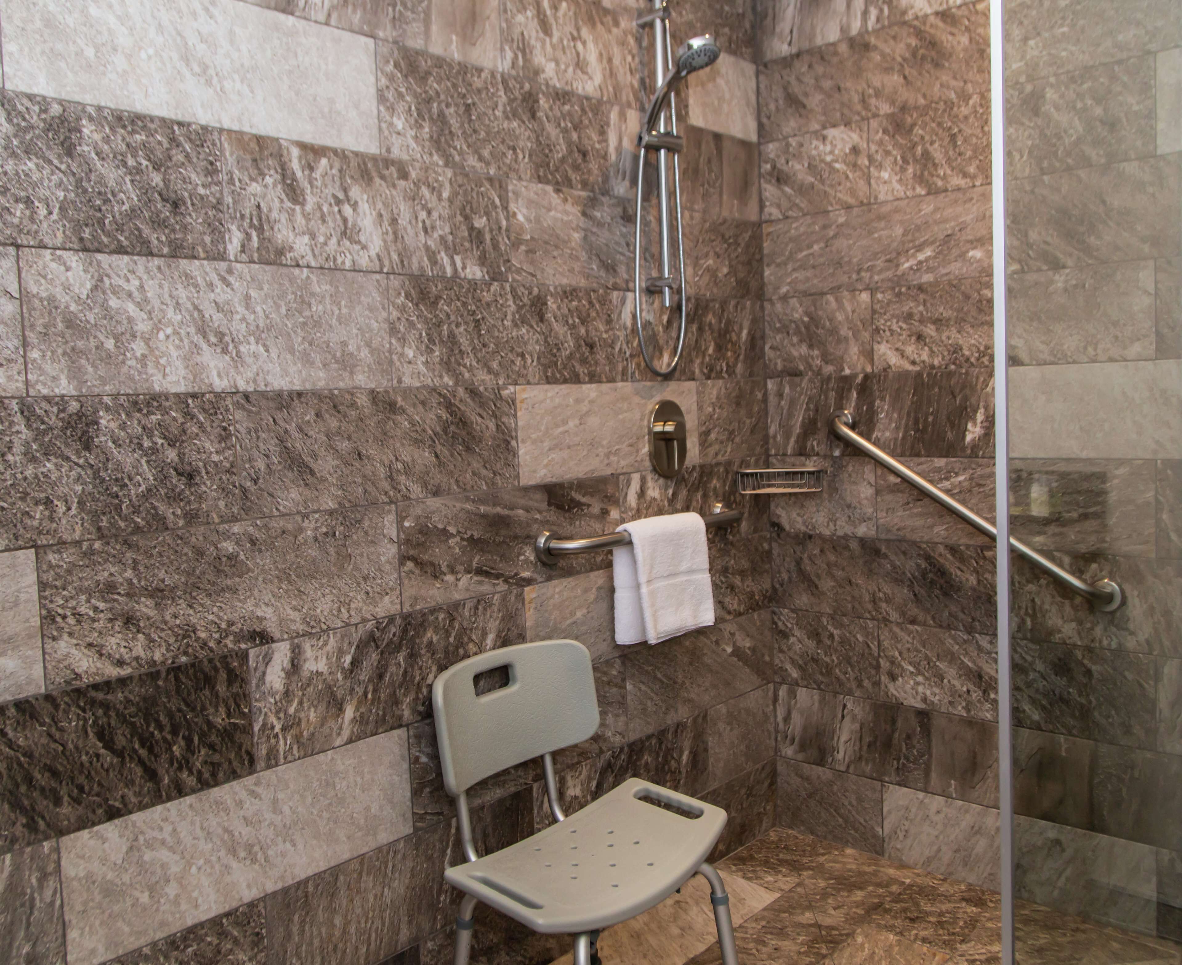 Un área de ducha con puerta de cristal, un pasamanos, un perchero y una silla.