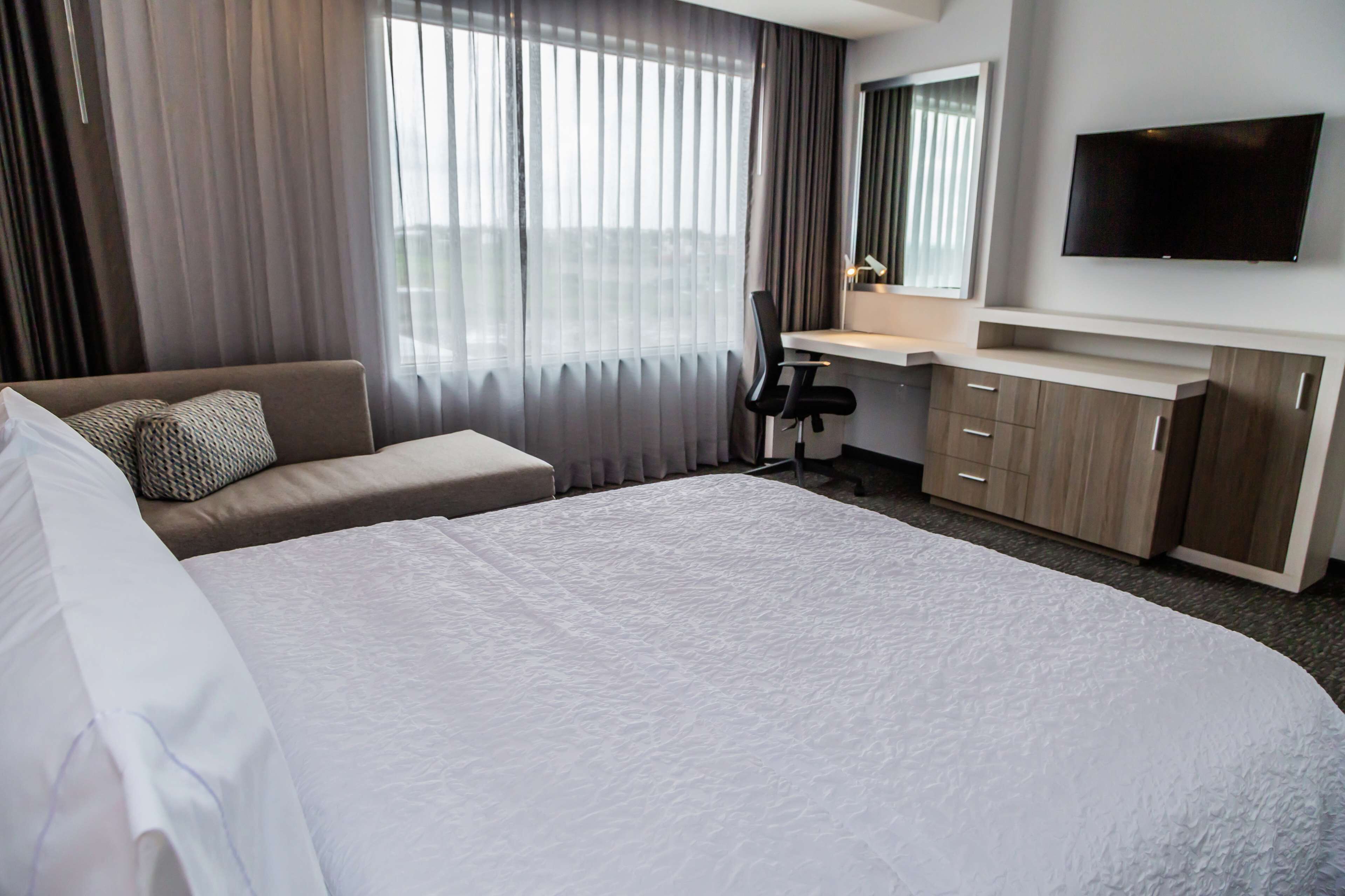 A hotel room with a large bed, a desk, a chair, a TV, and a window with curtains.