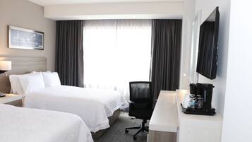 A hotel room with two beds, a desk with a coffee maker, a TV, and a window with curtains.