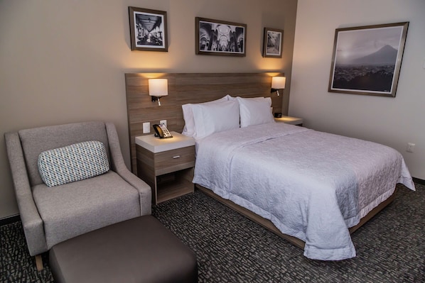 A hotel room with a bed, a chair, a nightstand, and a wall-mounted lamp. - Hampton Inn & Suites by Hilton Puebla (San Andrés Cholula)