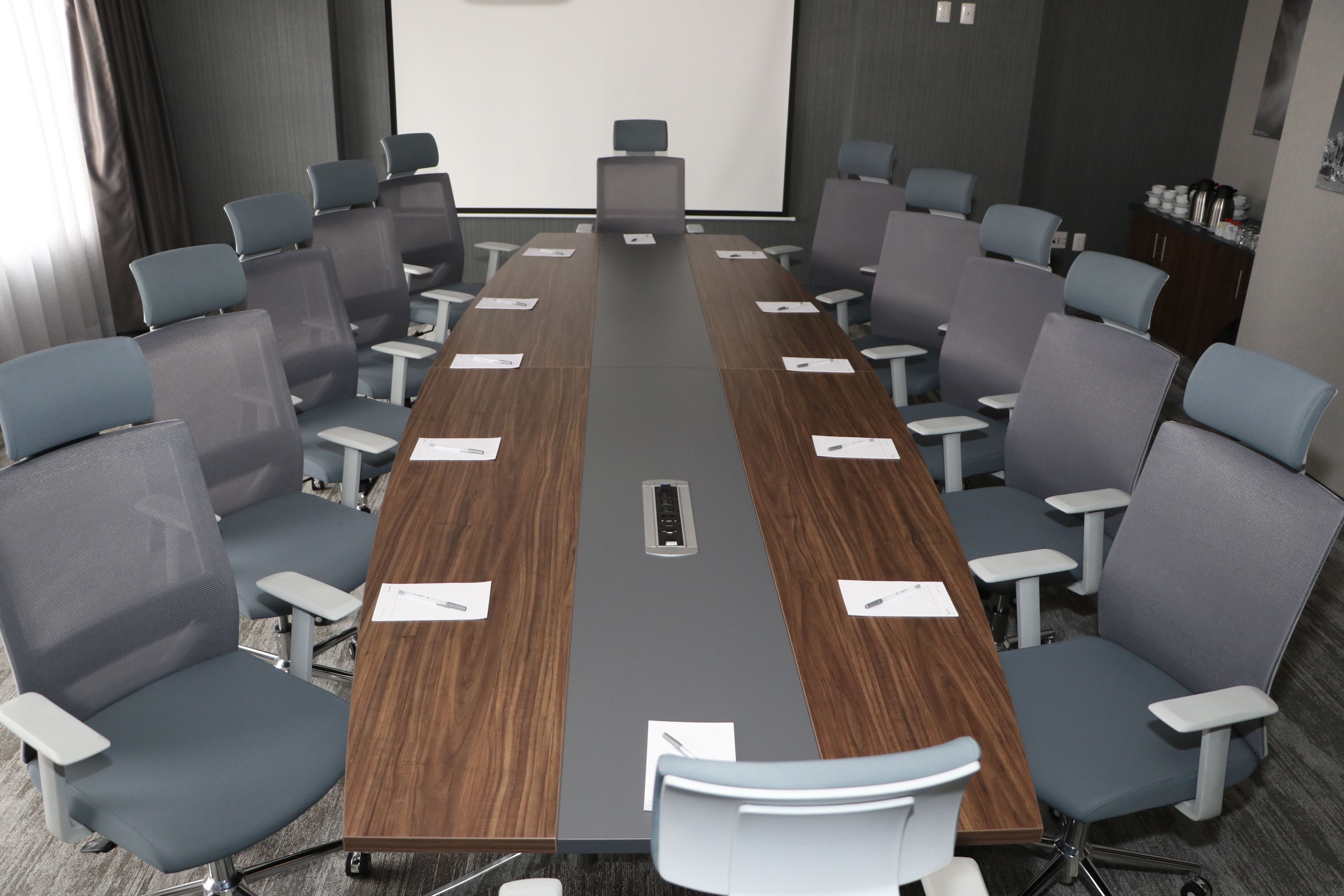 A conference room with a long table, multiple chairs, a projector screen, and a whiteboard.