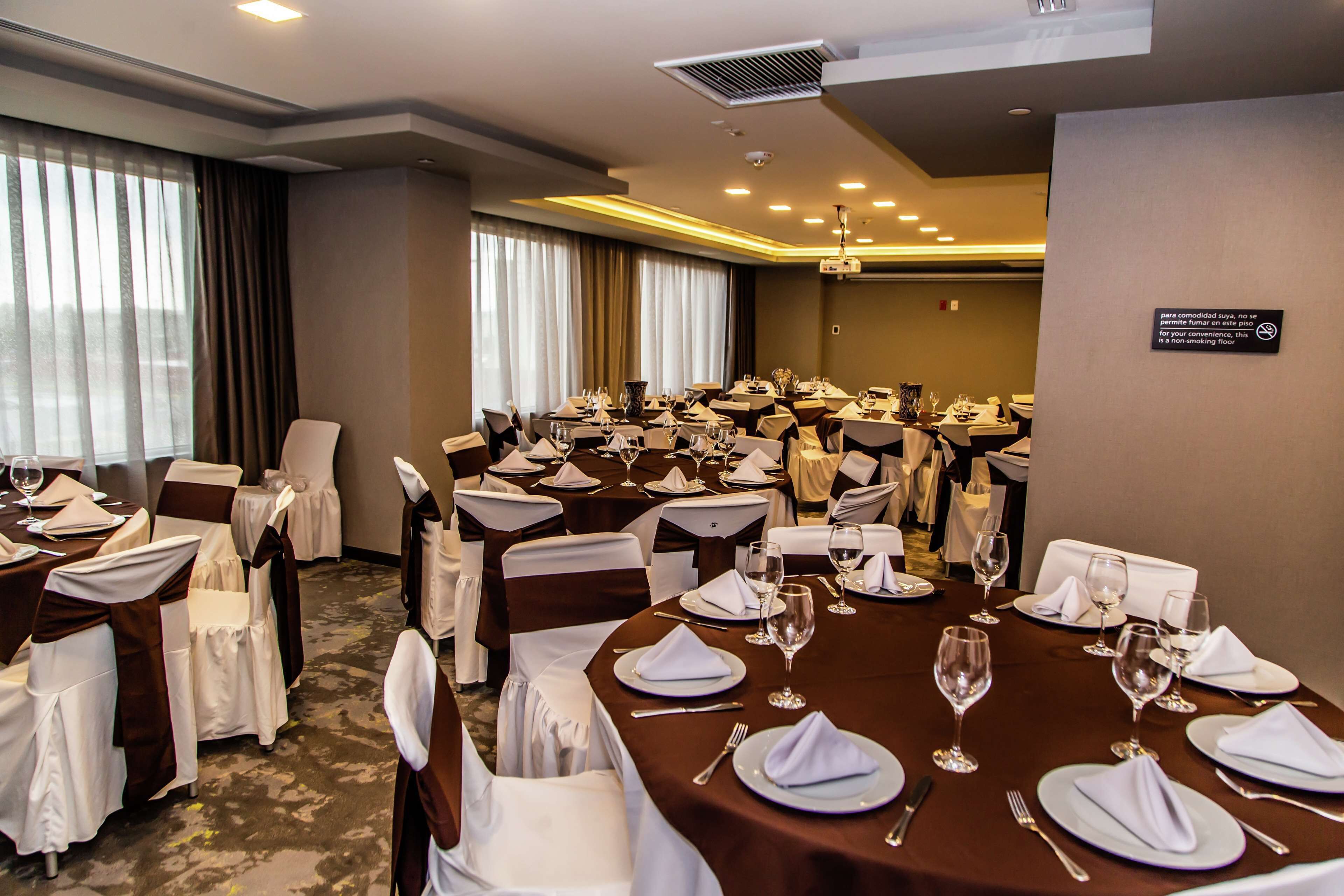 A conference room with round tables set for a formal event, equipped with chairs, tablecloths, and glassware.