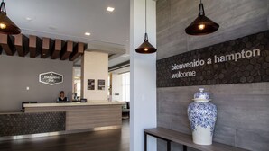 A reception area with a wooden reception desk, a large blue and white vase, and a sign that reads "bienvenido a Hampton welcome". - Hampton Inn & Suites by Hilton Puebla (San Andrés Cholula)