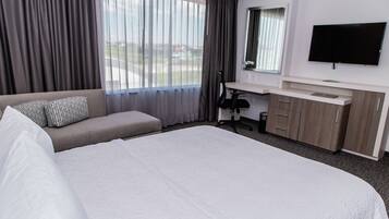 Habitación de hotel con una cama grande, un escritorio con silla, televisión y ventana con cortinas.