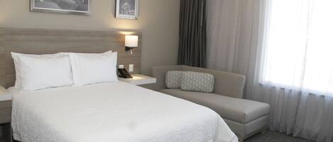 A hotel room with a large bed, a sofa, a nightstand, a lamp, and two framed pictures on the wall.