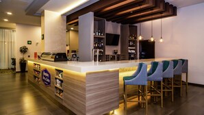 A modern bar area with a counter, bar stools, and shelves stocked with bottles. - Hampton Inn & Suites by Hilton Puebla (San Andrés Cholula)