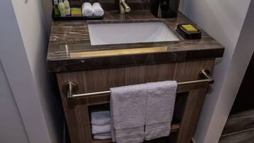 Un baño con encimera de mármol, un lavabo, toallero y estante con artículos de aseo.