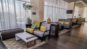 A modern hotel lobby with a sofa, armchairs, a coffee table, and a potted plant. - Hampton Inn & Suites by Hilton Puebla (San Andrés Cholula)