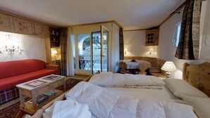 Habitación de hotel con una cama, un sofá rojo, una mesita con una lámpara y vistas al exterior a través de un ventanal.