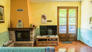 Ein Wohnzimmer mit Kamin, Fernseher und einem großen Fenster mit Blick ins Grüne.