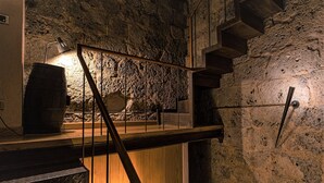 Een wenteltrap met metalen leuning die naar een hoger gelegen deel leidt, een houten vat en een stenen muur.