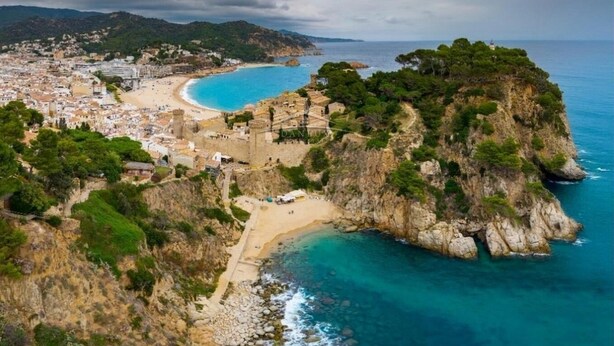 An aerial view of a coastal town with a beach, rocky cliffs, and a historic fortification.