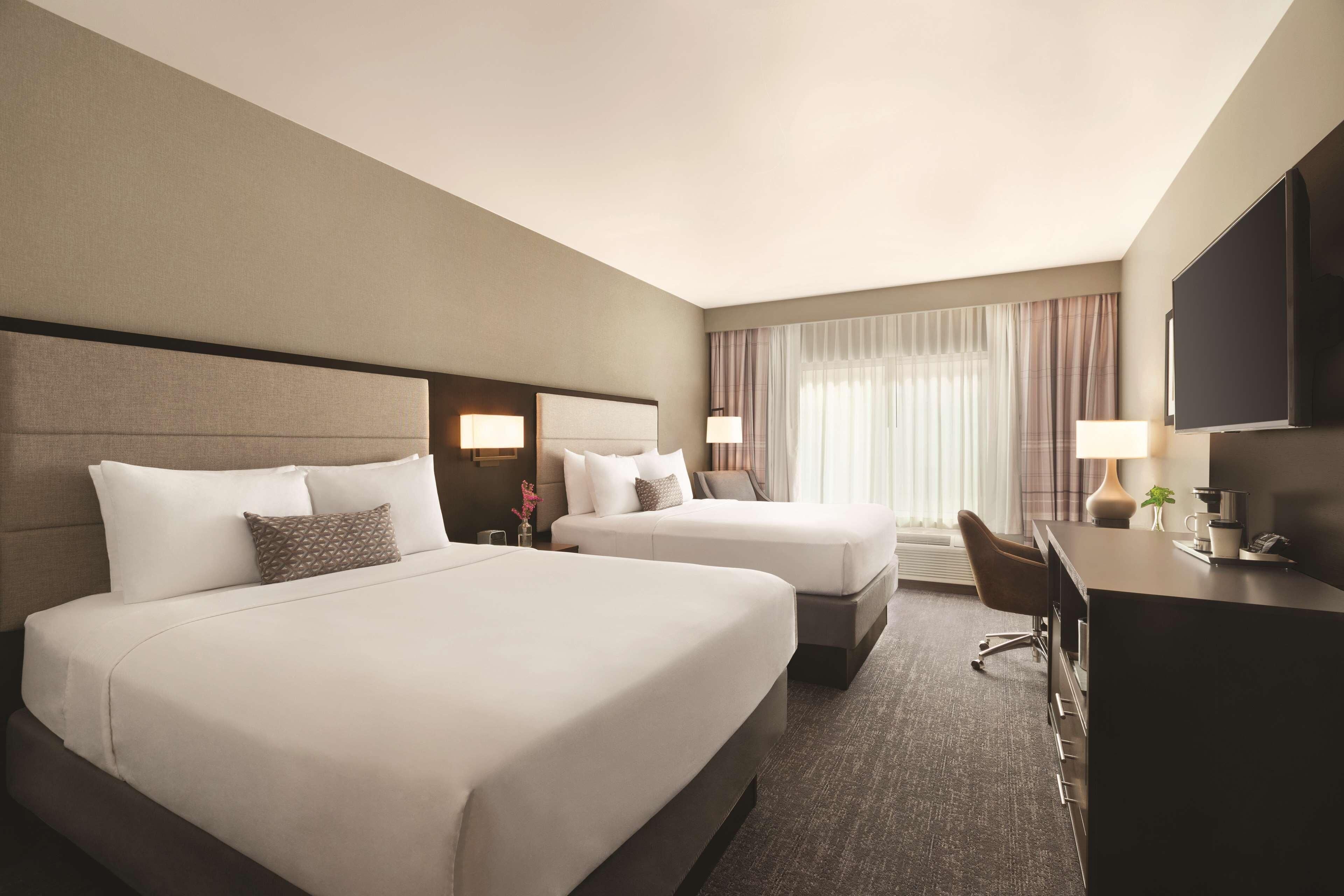 A hotel room with two beds, a desk, a chair, and a television.
