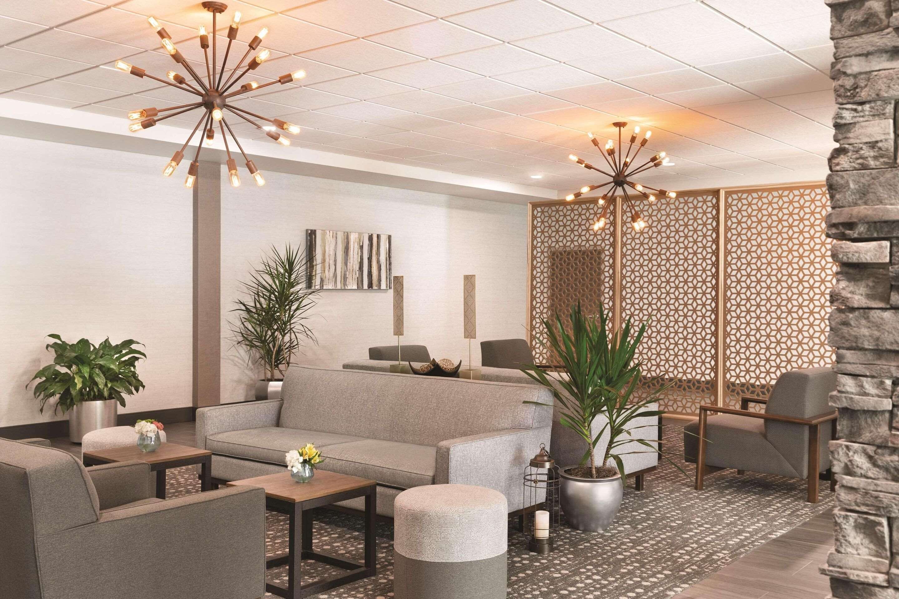 En moderne lobby med en grå sofa, lænestole, et sofabord og en dekorativ lampe.