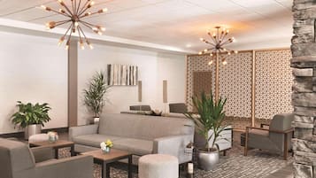 En moderne lobby med en grå sofa, lænestole, et sofabord og en dekorativ lampe.
