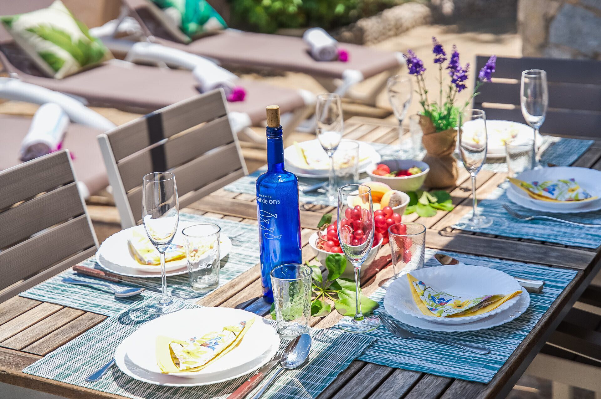 An outdoor dining table set with plates, glasses, and a blue bottle.