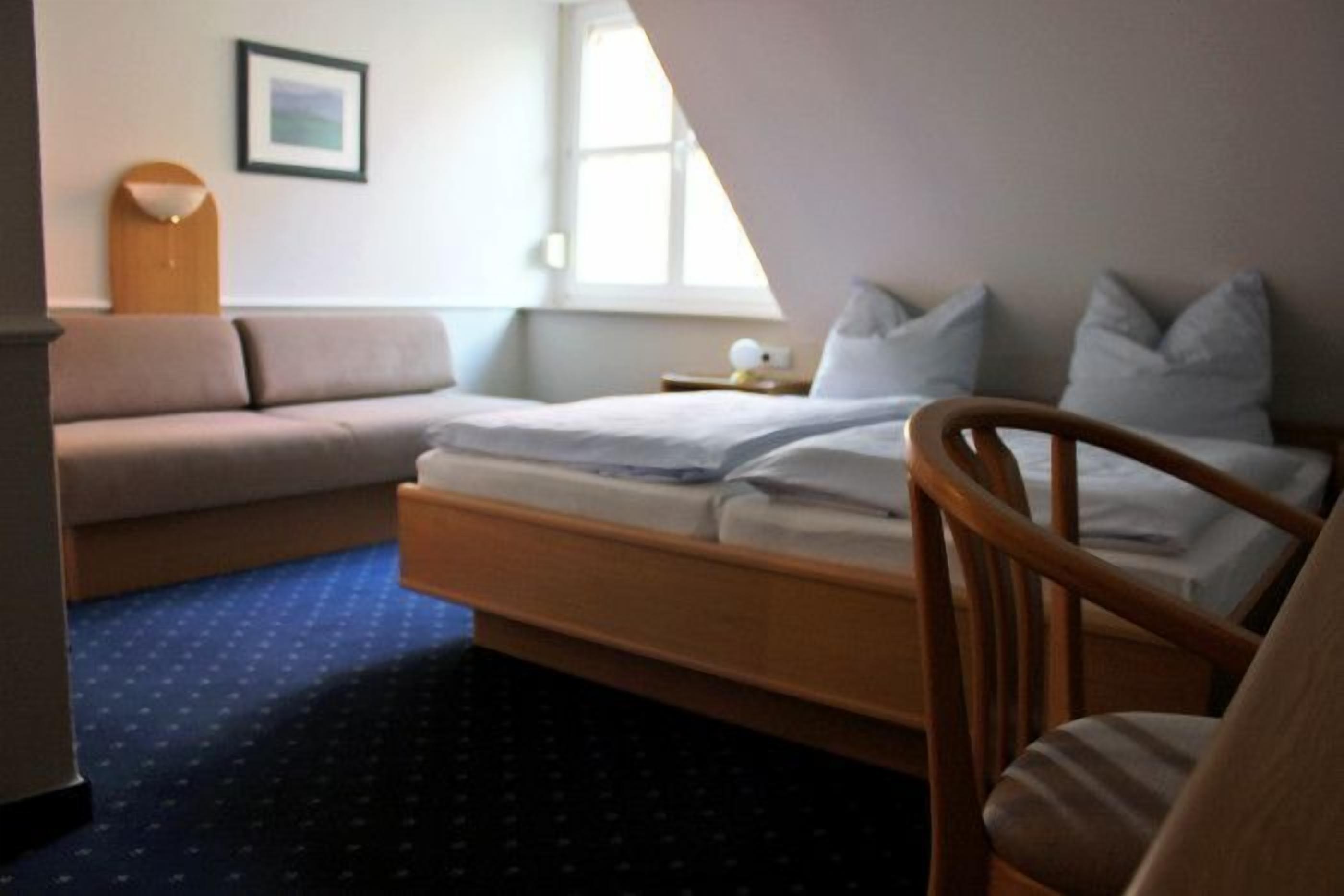Una camera da letto con un letto, una sedia di legno, un divano, un tavolino e un quadro appeso al muro.