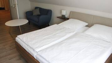 A bedroom with a double bed, a small round table, a blue armchair, and a bedside lamp.