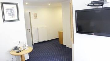 Ett hotellrum med en stor, platt-TV som är monterad på väggen, ett litet runt bord med en telefon och en lampa samt en mönstrad matta.
