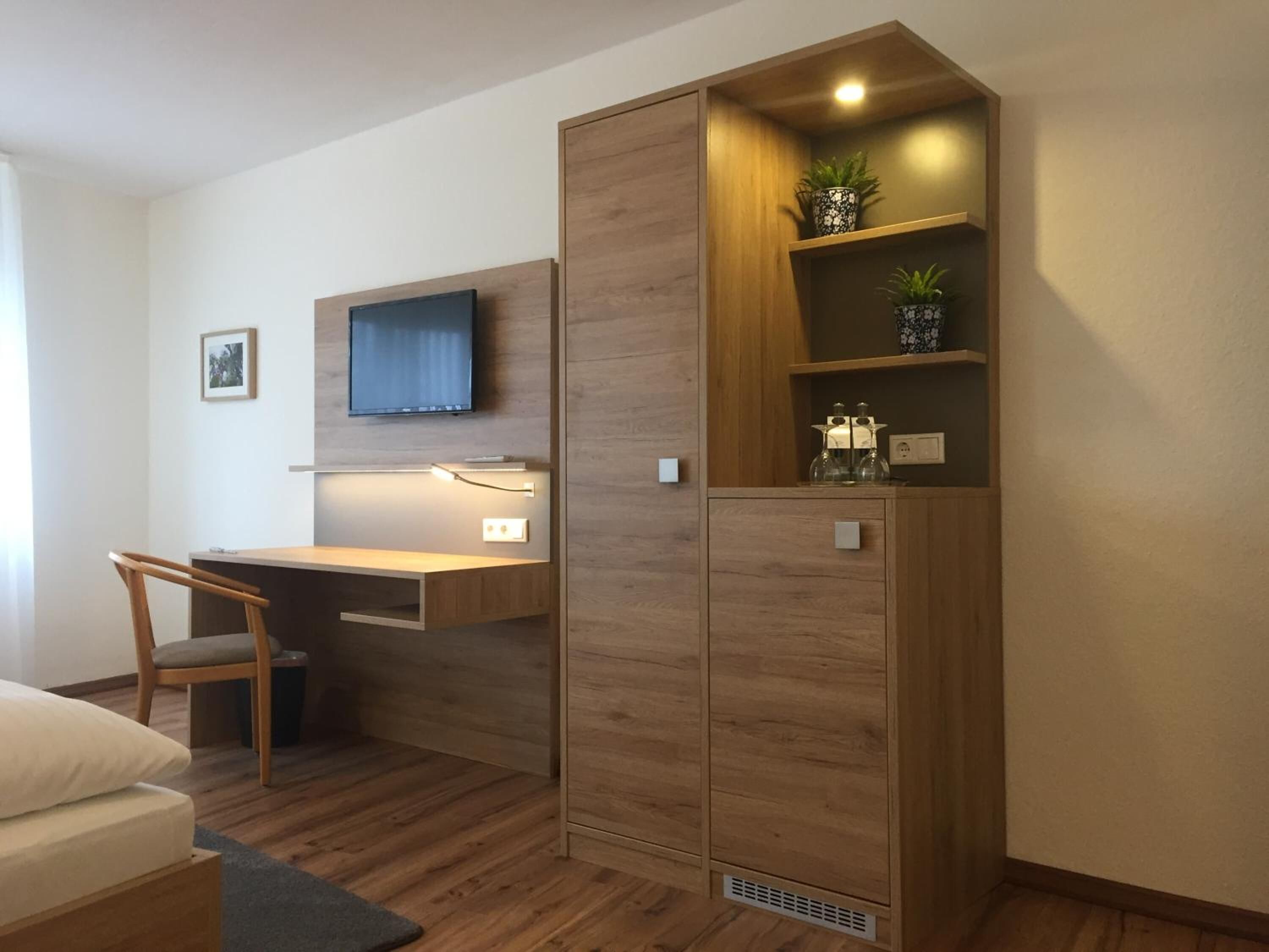 A modern bedroom with a wooden desk, a chair, a bed, and a wardrobe with shelves.
