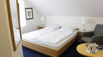 Habitación de hotel con una cama, dos mesitas de noche con lámparas, una silla y una pequeña mesa con una botella y un vaso.