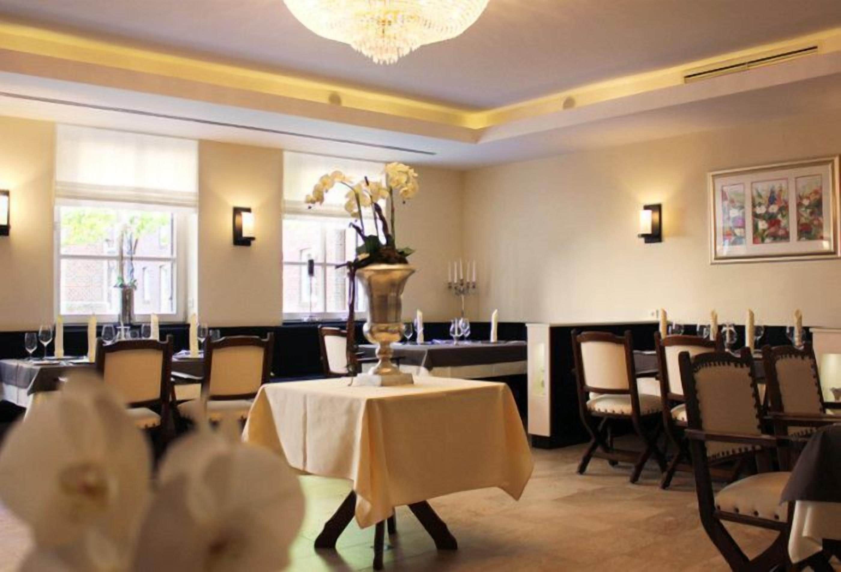A dining area with tables set for service, a chandelier, and wall-mounted lighting.