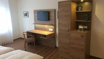 Habitación de hotel con cama, escritorio, silla, televisor montado en la pared y armario con estantes.