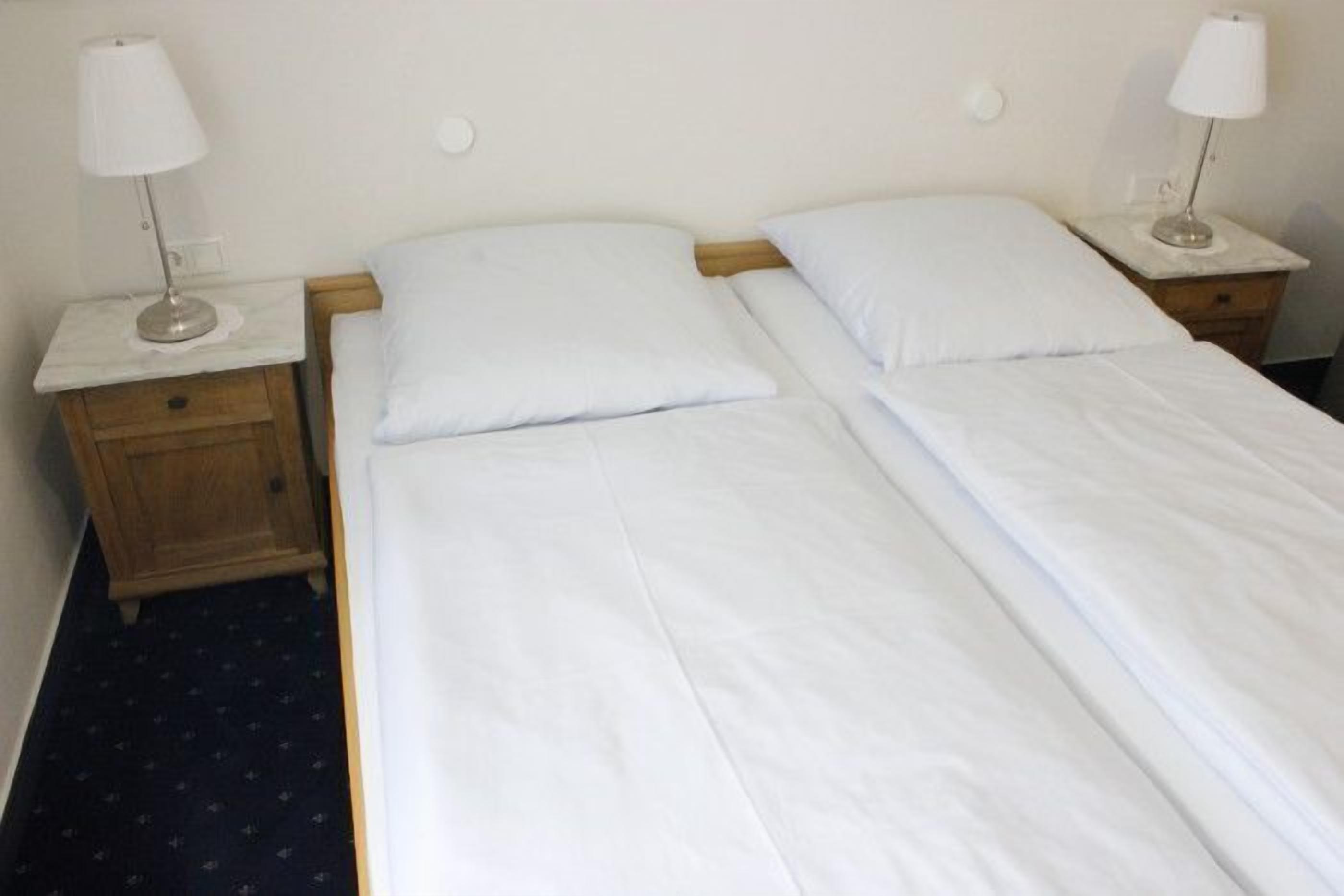 A double bed with white linens, two bedside tables with lamps, and a wooden nightstand.