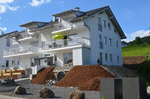 A two-story building with balconies, a covered outdoor seating area, and a large pile of mulch in the foreground. - 4 **** apartment EdelWeiß, 3 rooms, underground parking, elevator, WiFi, Oberstaufen Plus (Oberstaufen)