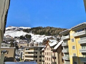 A multi-story building with balconies, likely a hotel, in a snowy mountainous area with clear skies.