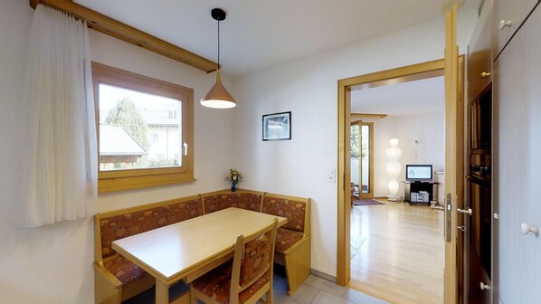 A dining area with a wooden table and bench, a pendant light, a window with curtains, and a framed picture on the wall.