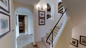 Eine Treppe mit Holzdielen und schwarzen Geländern, die zu einem Raum mit weißen Wänden und gerahmten Bildern führt.
