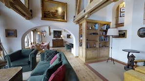 A cozy living room with a green sofa, a wooden bookshelf, and a dining area with a table and chairs. - Very spacious, tastefully furnished 5-room-maisonette-apartment with a big balco (Champfèr)
