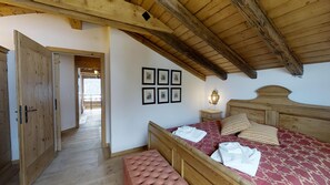 Um quarto com cama de madeira, um banquinho, mesa de cabeceira com abajur e quadros na parede.