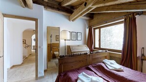 Ein Schlafzimmer mit einem hölzernen Bett, einem Fenster mit Vorhängen, einer Nachttischlampe und Blick ins Freie.