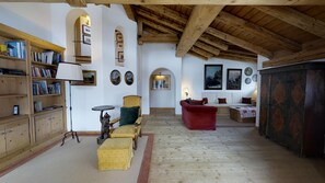 Um quarto aconchegante com teto de madeira, estante de livros, poltrona amarela, sofá vermelho e um armário estampado.