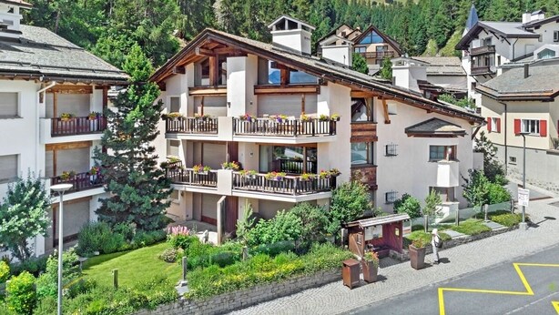 Ein mehrstöckiges Hotel mit Balkonen, umgeben von üppiger Vegetation und einer Bergkulisse.