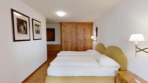 A hotel room with two beds, wooden wardrobe, framed pictures on the wall, and a bedside lamp.