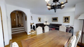 A dining area with a wooden table and chairs, a staircase leading to another room, and a chandelier.