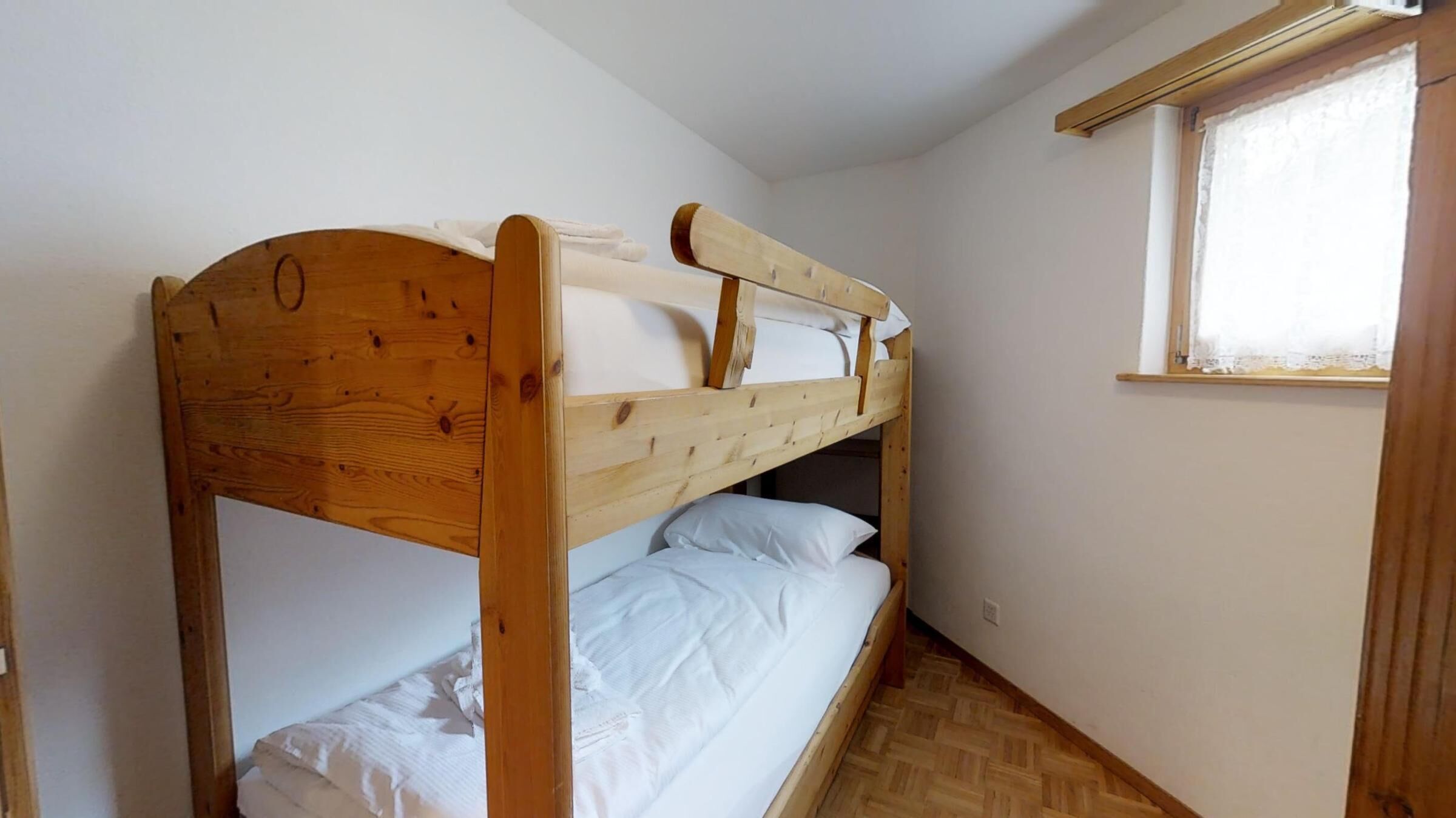A bunk bed in a room with a window, wooden flooring, and white walls.
