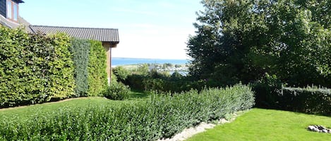 A well-maintained garden with a lawn, two black lounge chairs, and a view of the sea in the background.