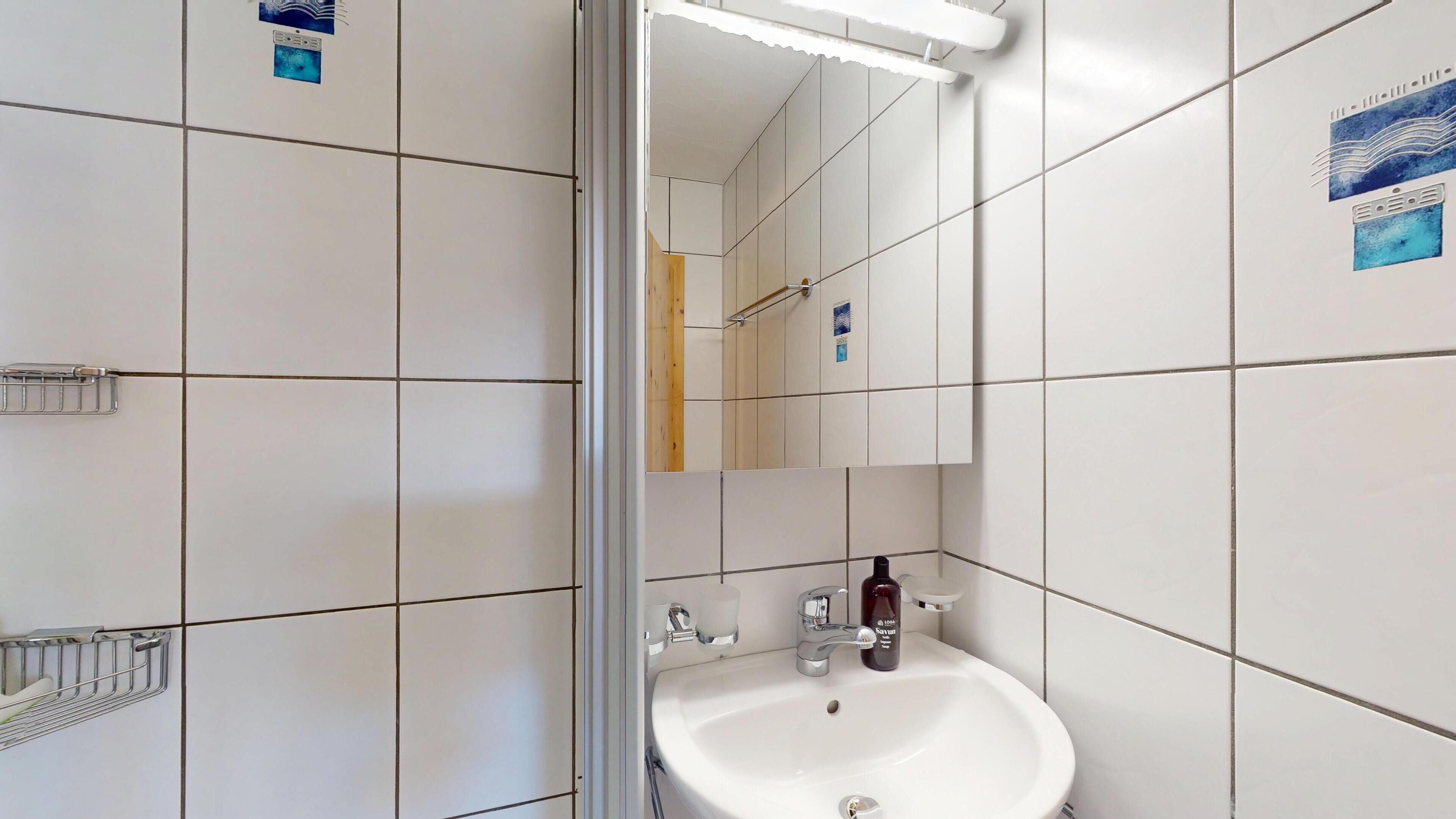 Une salle de bain avec des murs carrelés de carreaux blancs, un lavabo avec un miroir au-dessus et un porte-serviettes.