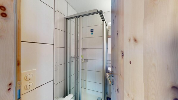 A bathroom with white tiled walls, a glass shower enclosure, and a wooden floor.