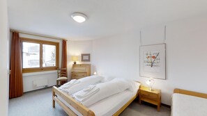 Une chambre à coucher avec un lit en bois, une table de chevet, une commode, une fenêtre avec des rideaux et un tableau encadré au mur.