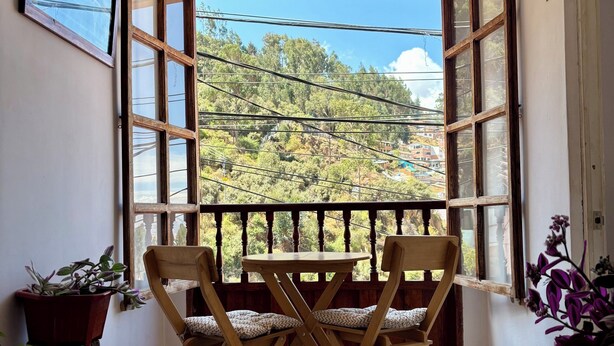 A balcony with wooden chairs and a table, potted plants, and a view of a hillside. - Big Vacation Hostel (Cusco)