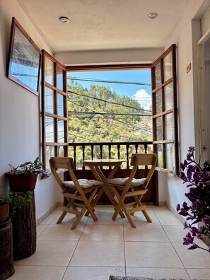 A balcony with wooden chairs and a table, potted plants, and a view of a hillside. - Big Vacation Hostel (Cusco)