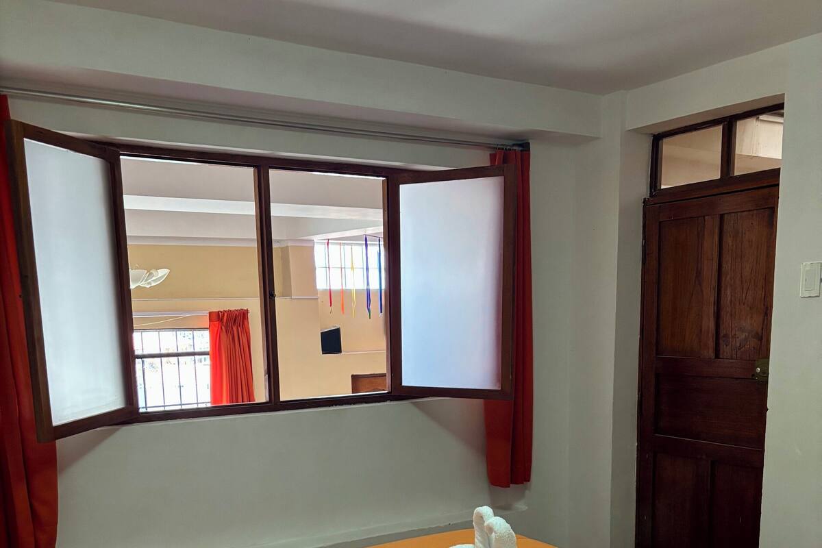A hotel room with an orange bedspread, a wooden door, and a window with curtains.