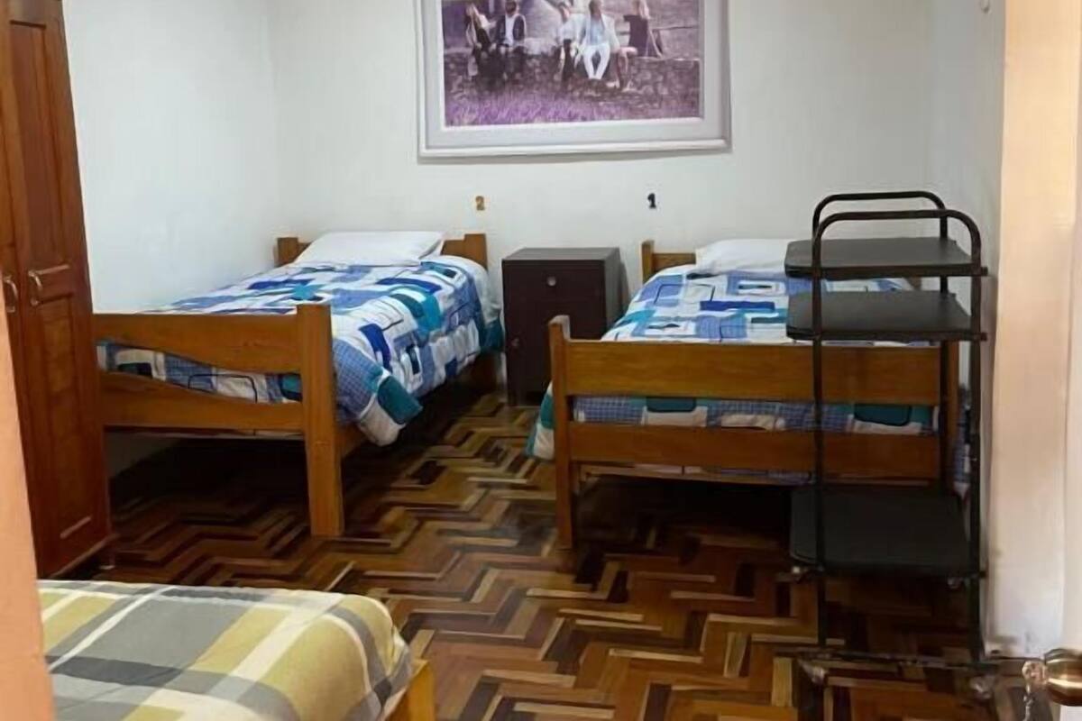 A dormitory room with two bunk beds, a wooden wardrobe, a small desk, and a framed picture on the wall.