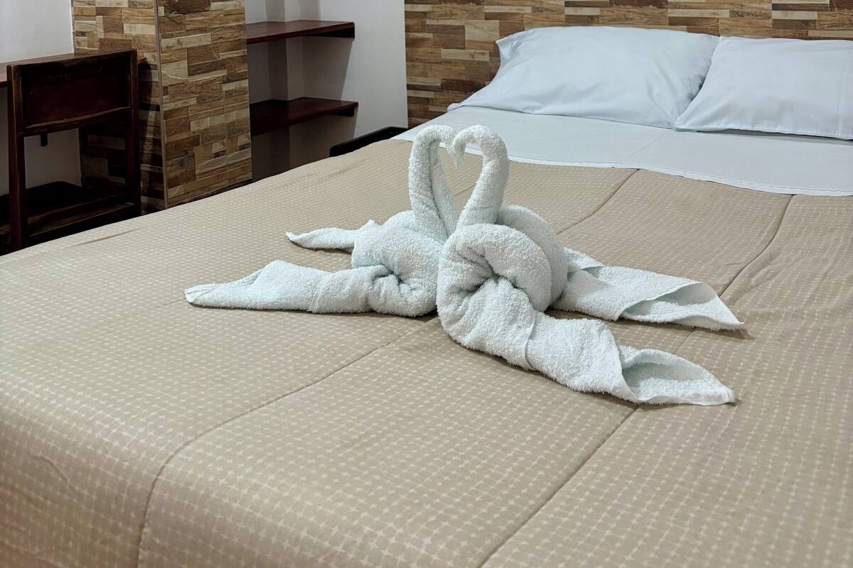 A hotel room with a bed, a wooden wall panel, a hanging coat rack, and a bedside table.