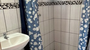 A bathroom with a white sink, tiled walls, and a shower area with blue curtains featuring a pattern. - Big Vacation Hostel (Cusco)